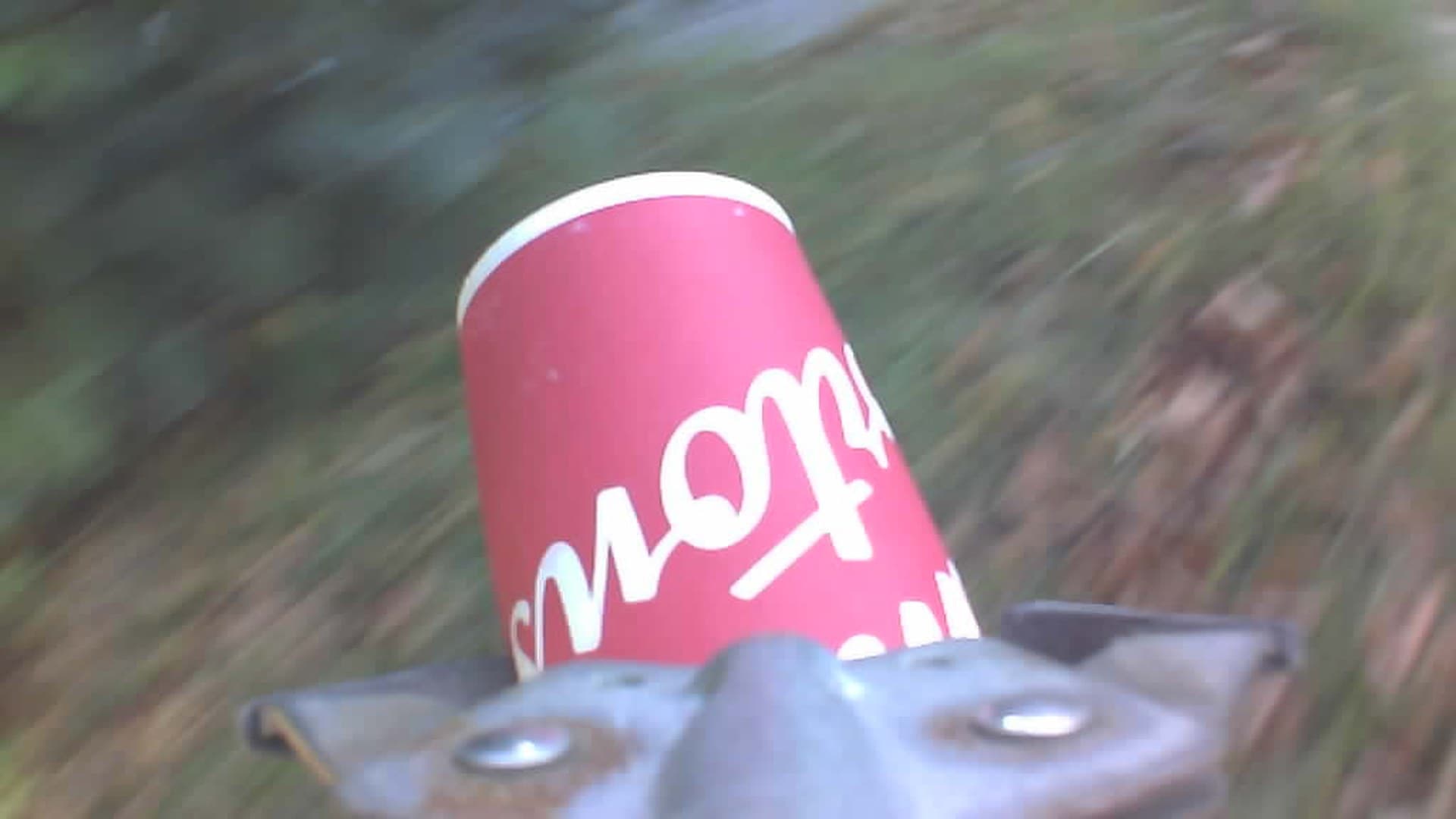 A red paper coffee cup on asphalt ahead of the picker’s jaws, seen from the camera mounted on the picker.