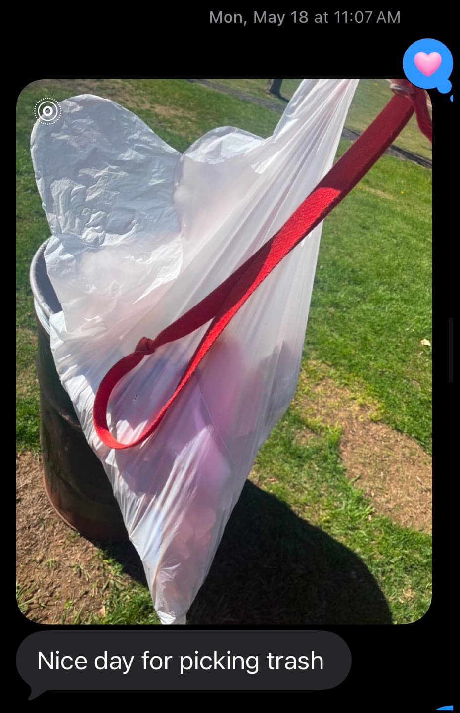 A text with a photo of a full white bag of litter hung on a park bin in the sun, reading “Nice day for picking trash”.
